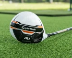 TaylorMade R1 white driver head resting on green practice turf showing racing stripe graphics